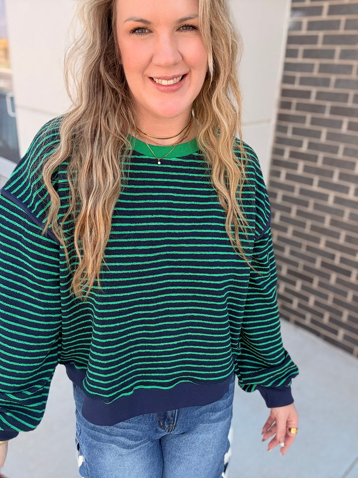 A woman wearing a dark green and navy blue horizontally striped long-sleeve sweatshirt with solid green and navy trim, paired with blue jeans.