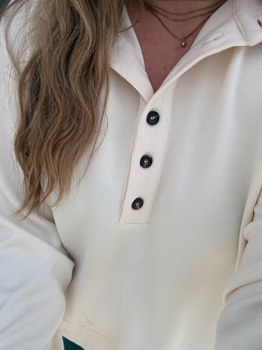 Close-up of a person wearing a cream ribbed knit long-sleeve polo shirt with a three-button placket and dark buttons.