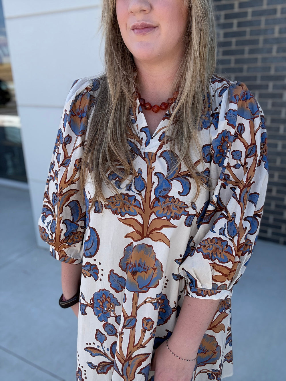 A woman wearing a cream-colored blouse with a brown and blue floral block print, standing outdoors in front of a building.